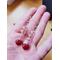 Earrings rest on a person's hand. Shows the pink beads' transparency and the red charms' darkness. Stripes on heart charms barely visible.